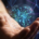 Gros plan d'une main tenant une sphère numérique lumineuse avec un réseau global de points connectés, sur fond sombre.