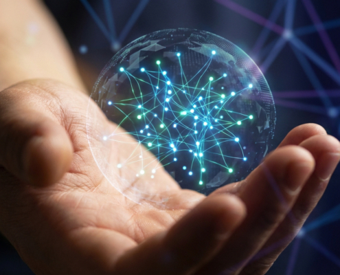 Gros plan d'une main tenant une sphère numérique lumineuse avec un réseau global de points connectés, sur fond sombre.